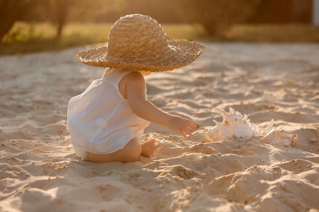 Niña en ropa blanca jugando en una playa de arena en verano