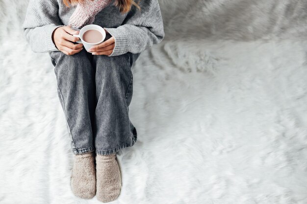 Una niña con ropa de invierno disfrutando de una taza de chocolate caliente en la temporada de invierno en casa