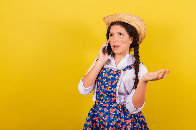 Niña con ropa típica de Festa Junina en llamada de voz móvil llamada conectada Para la fiesta de Arraia