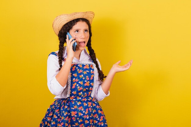 Niña con ropa típica de Festa Junina en llamada de voz móvil llamada conectada Para la fiesta de Arraia