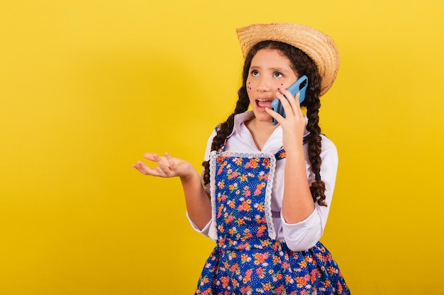 Niña con ropa típica de Festa Junina en llamada de voz móvil llamada conectada Para la fiesta de Arraia