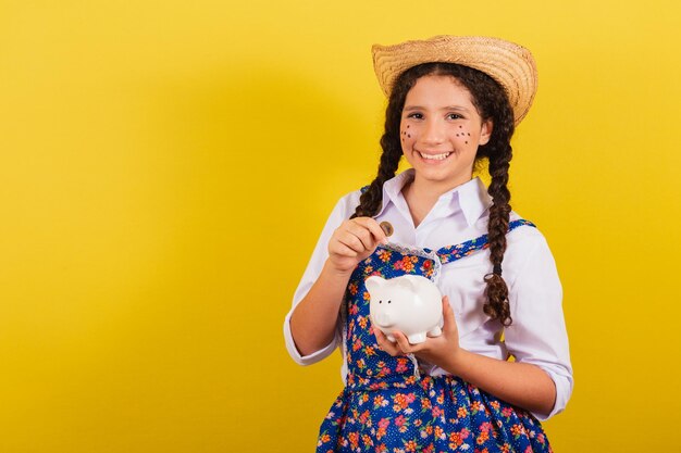 Niña con ropa típica de Festa Junina Sosteniendo moneda y alcancía Para la fiesta de Arraia