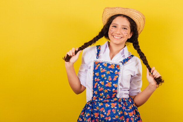 Niña con ropa típica de Festa Junina sosteniendo trenzas y sonriendo para el Festival do Arraia