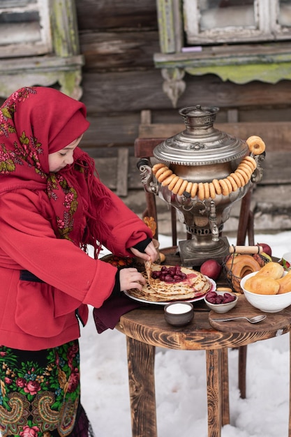 Una niña con ropa tradicional con una pila de panqueques, samovar. Maslenitsa.
