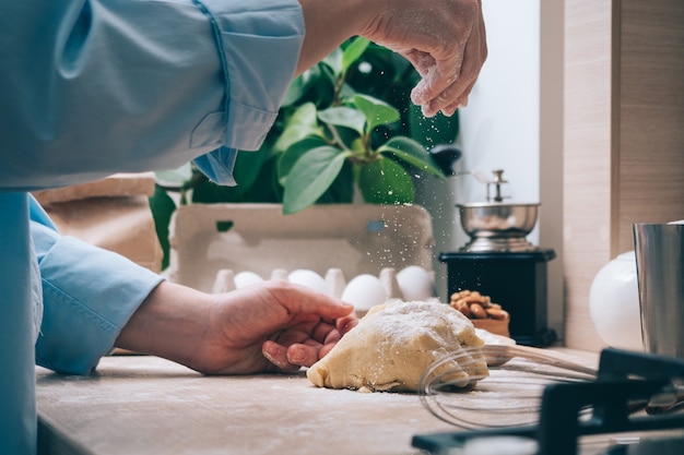 Una niña sin rostro prepara la masa, la espolvorea con harina, primer plano. Cocinar pasteles caseros en la cocina, en casa. Fondo culinario.