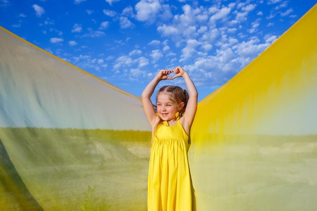 Una niña rubia de 7-8 años con un vestido amarillo brillante contra un cielo azul.