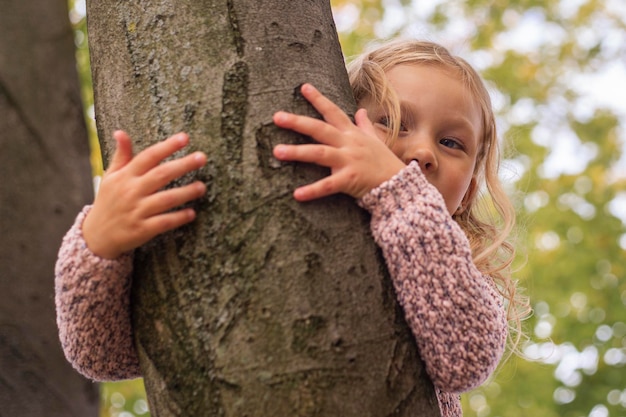 Niña rubia abrazando con las dos manos un árbol en el parque