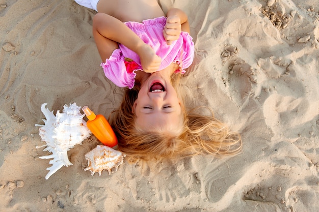 Niña rubia acostada en una playa de arena sonriendo