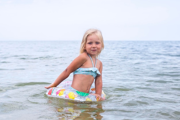 Niña rubia con un anillo inflable se baña en el mar.