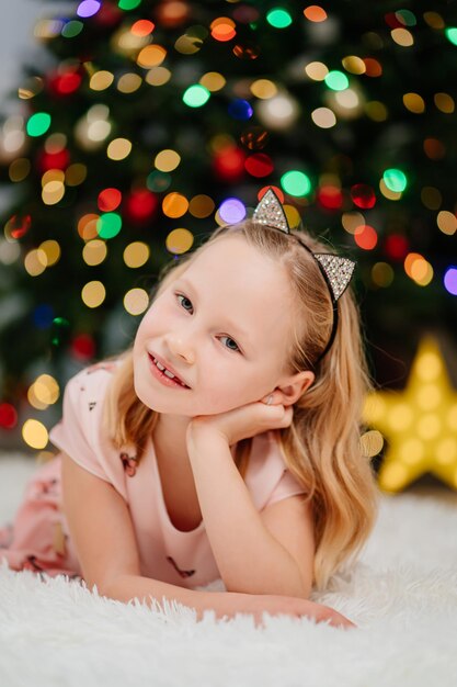 Niña rubia bonita y feliz en vestidos de color rosa en el árbol de navidad