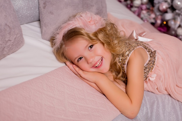 Foto niña rubia en la cama junto al árbol de navidad. nochebuena