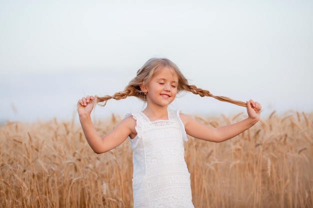 Niña rubia camina en un campo de trigo de verano