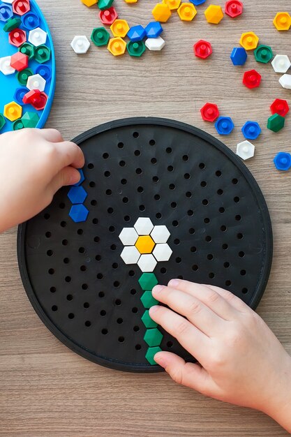 Foto niña rubia con una camiseta blanca jugando con mosaico multicolor de plástico en casa o preescolar.