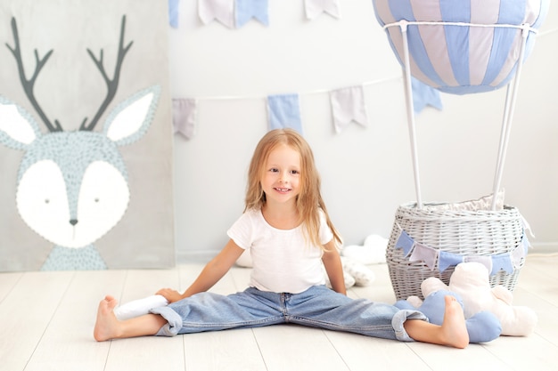 Niña rubia en una camiseta y jeans se sienta cerca de un globo decorativo. Niño divertido juega cerca del globo en la habitación de los niños. El concepto de infancia, creatividad. cumpleaños, decoraciones navideñas