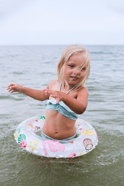 Niña rubia con un círculo se juega en el mar