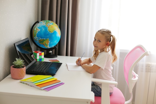 Niña rubia colegiala en casa enseña lecciones de educación en línea portátiles portátiles globo