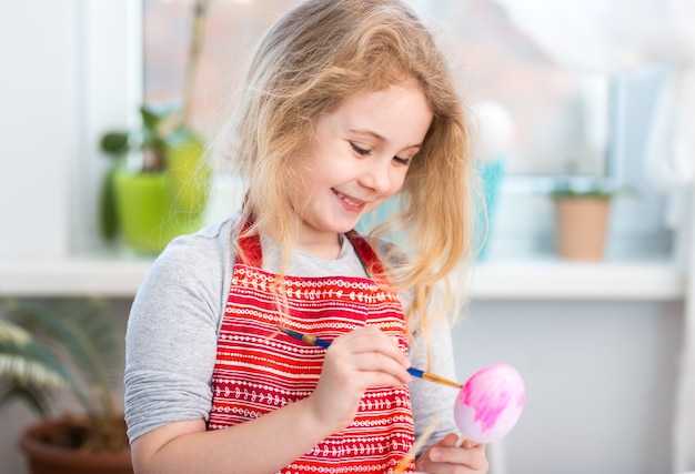 Niña rubia coloreando huevos para las vacaciones de Pascua en casa.