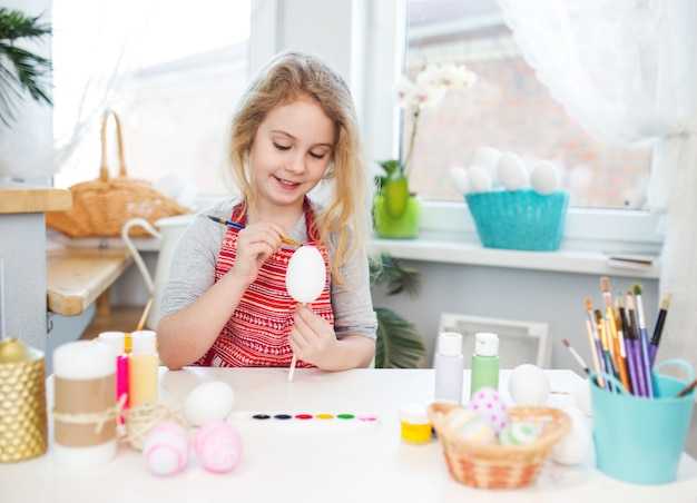 Niña rubia coloreando huevos para las vacaciones de Pascua en casa.