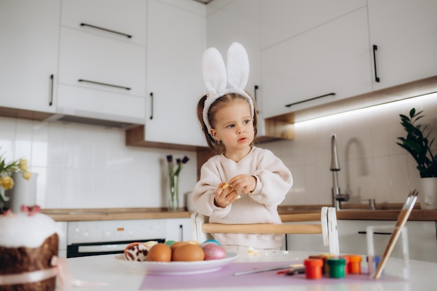 Niña rubia coloreando huevos para las vacaciones de Pascua en casa