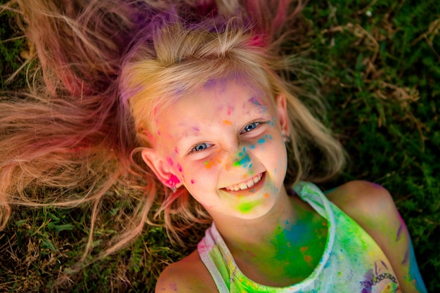 niña rubia en colores Holi sonriendo tirado en el pasto