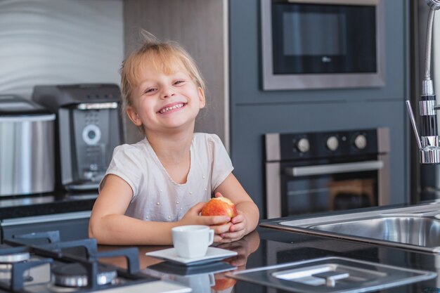 Niña rubia comiendo una manzana en la cocina