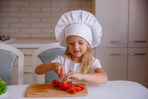 Niña rubia comiendo verduras en la cocina