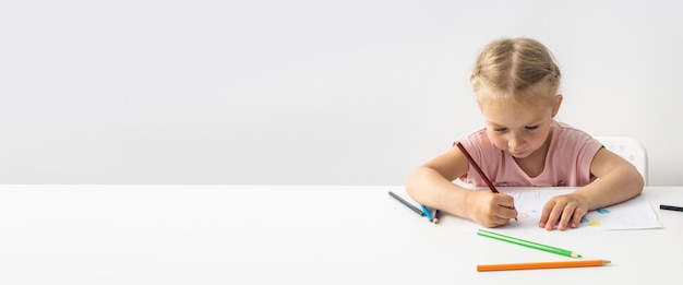 Niña rubia dibuja con lápices de colores sentados en la mesa Banner