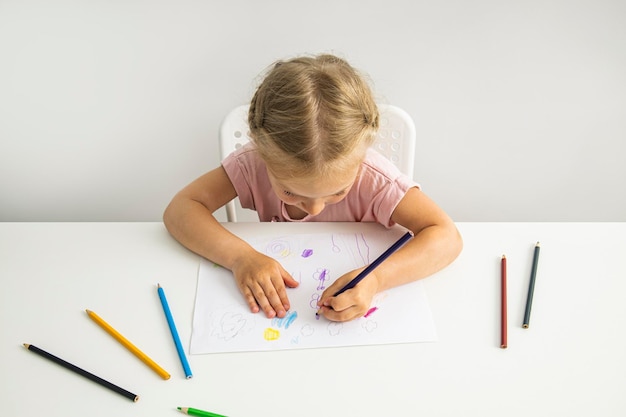 Niña rubia dibuja con lápices de colores sentados en la mesa Vista superior endecha plana