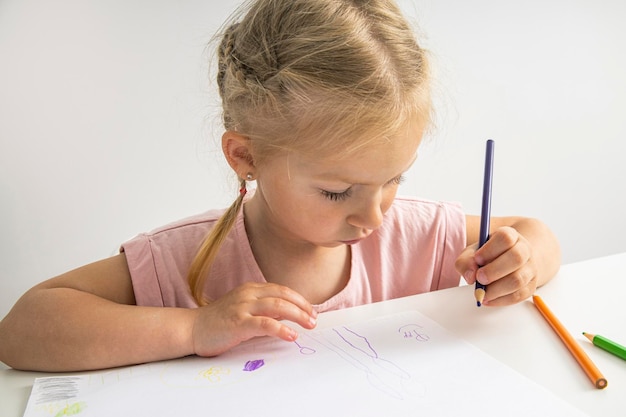 Una niña rubia dibuja con lápices de colores sentados en la mesa