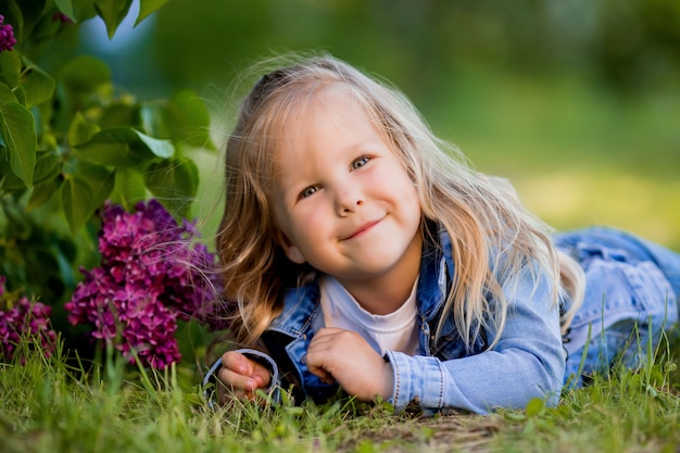 Niña rubia se encuentra cerca de las flores de color lila en la hierba verde y sonrisas