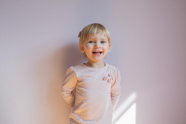 Una niña rubia feliz se apoya contra la pared en una habitación soleada en casa
