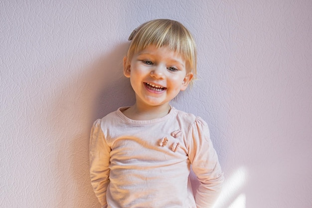 Una niña rubia feliz se apoya contra la pared en una habitación soleada