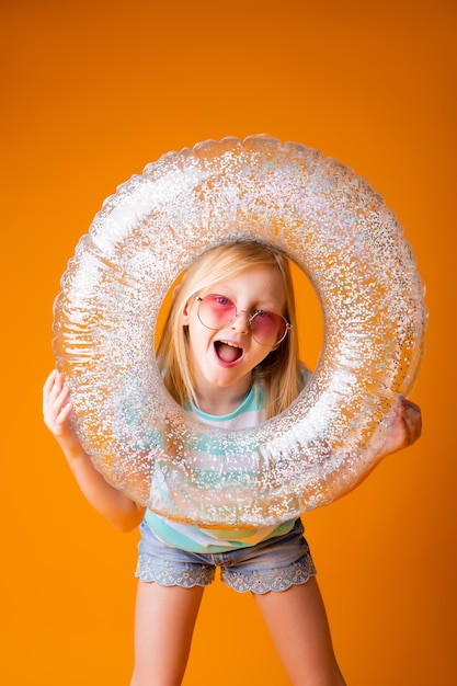 Niña rubia con gafas de sol tiene un círculo de natación en sus manos