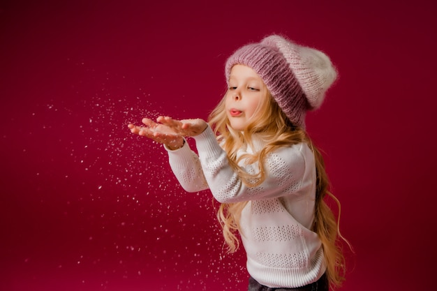 Niña rubia con gorro de punto y suéter juega con la nieve