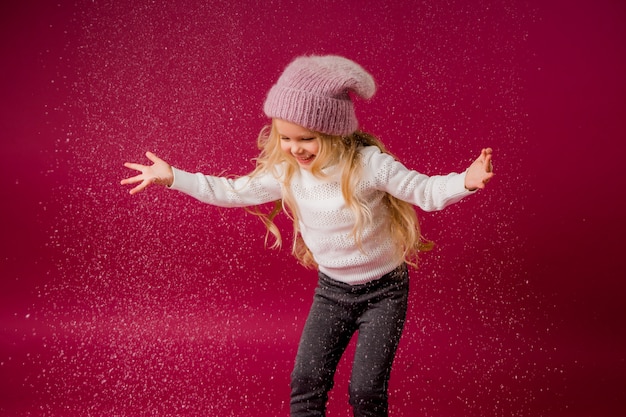 Niña rubia con gorro de punto y suéter juega con la nieve