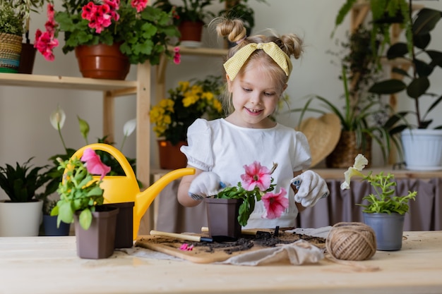 Niña rubia con guantes de trabajo, plantas y trasplantes y aguas de flores de interior