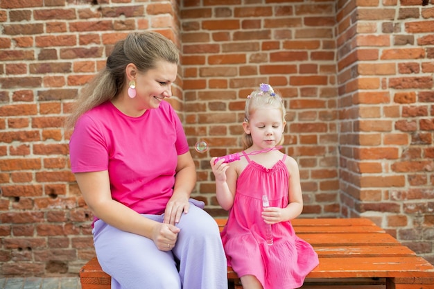 Foto niña rubia con implante coclear jugando con su madre al aire libre con discapacidad auditiva sordo y