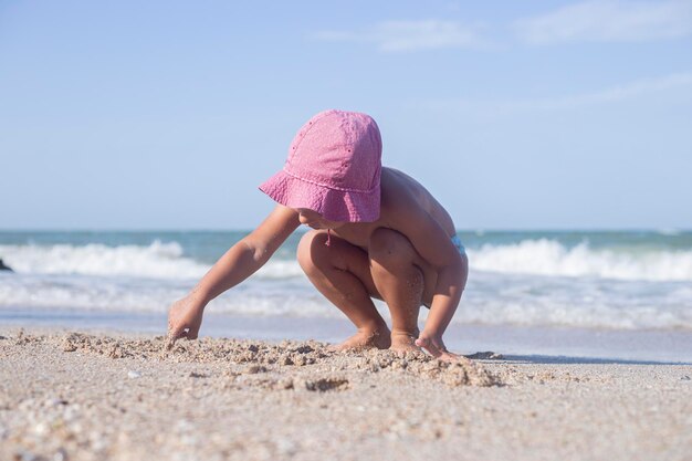 La niña rubia se juega con arena en la playa.