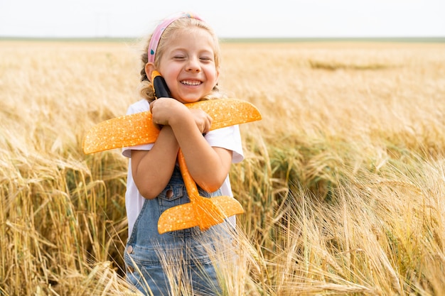 Niña rubia juega avión en el campo de centeno, cosecha de grano.