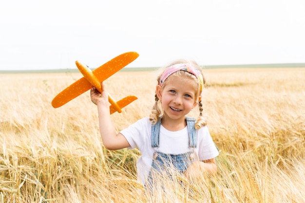 Niña rubia juega avión en el campo de centeno, cosecha de grano.