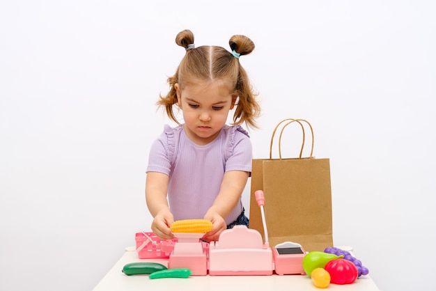 La niña rubia juega en la tienda pesa el maíz en una báscula de juguete recoge el pedido en un paquete artesanal caja registradora para niños juegos en el hogar para niños pedidos de comida en línea entrega de comida