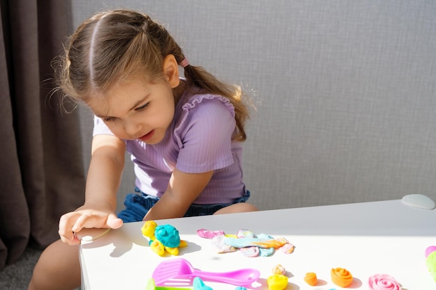 Niña rubia juega con tortuga hecha de plastilina en mesa blanca en juegos de casa con concepto de plastilina en casa