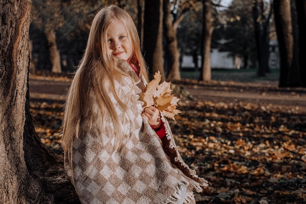 Niña rubia en un látigo a cuadros en el parque en otoño