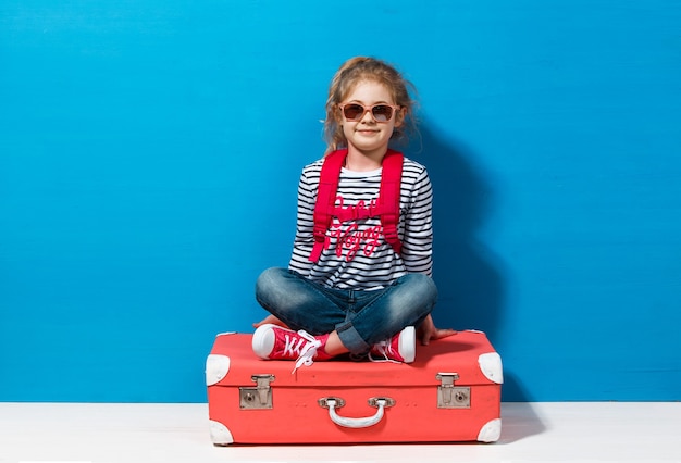 Niña rubia con maleta vintage rosa lista para las vacaciones de verano. Concepto de viajes y aventuras.
