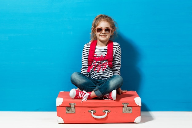 Niña rubia con maleta vintage rosa lista para las vacaciones de verano. Concepto de viajes y aventuras.