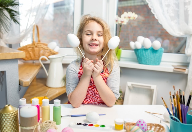 Niña rubia mostrando huevos antes de colorear para las vacaciones de Pascua en casa.