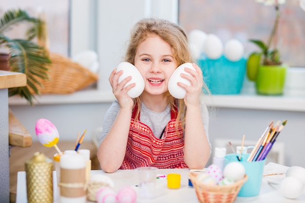 Niña rubia mostrando huevos antes de colorear para las vacaciones de Pascua en casa.