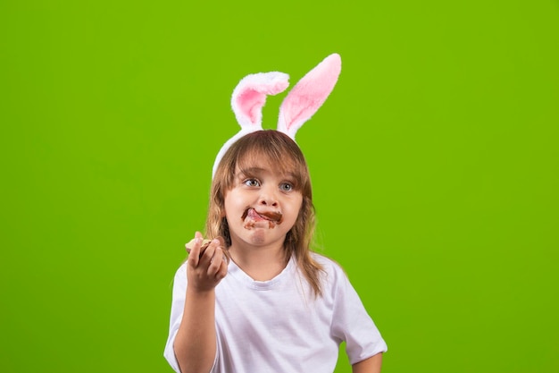 Niña rubia con orejas de conejo de chocolate sucias comiendo huevo de Pascua