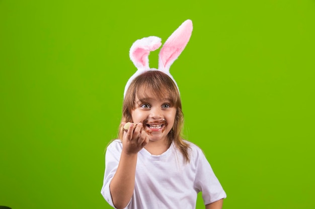 Niña rubia con orejas de conejo de chocolate sucias comiendo huevo de Pascua