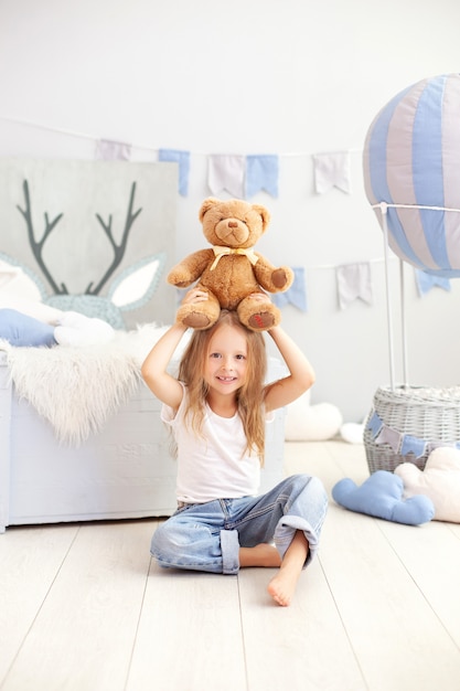 Niña rubia con un oso de peluche en la pared de un globo decorativo. El niño juega en la habitación de los niños con juguetes. El concepto de infancia, viaje. Niño en el jardín de infantes. interior